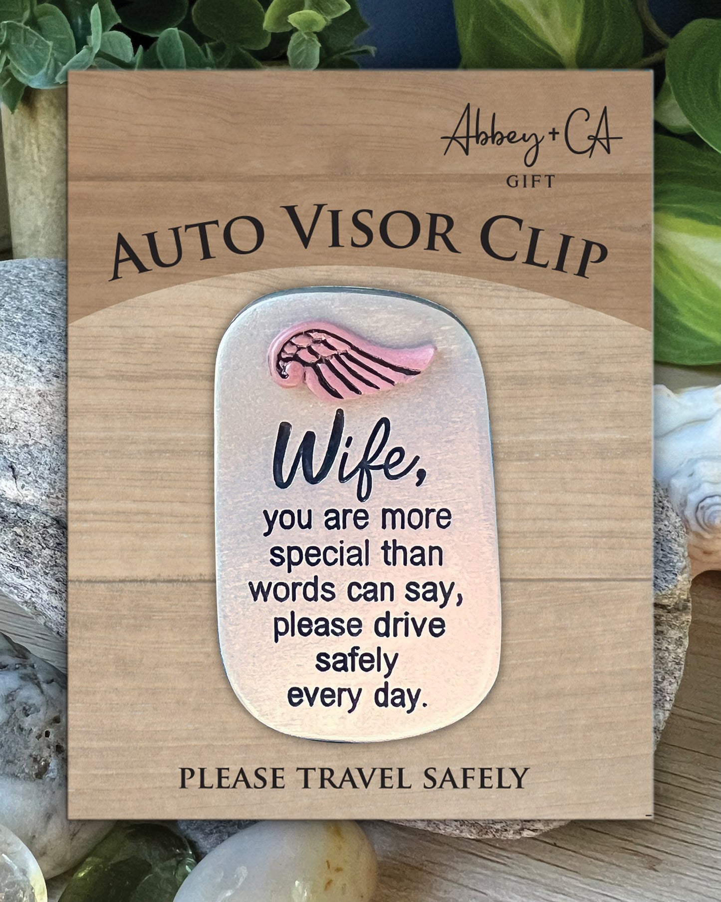 Auto visor clip with message on a wooden card, surrounded by natural elements.