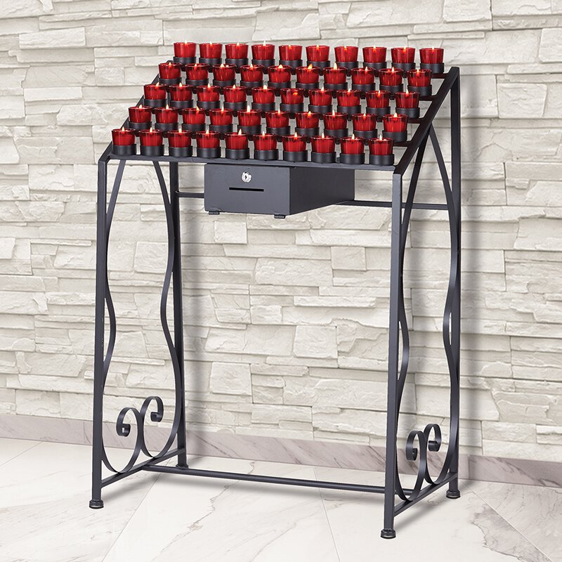 A traditional wrought iron 50-cup Devotional votive candle stand, with red candles placed on it, set against a brick wall backdrop.