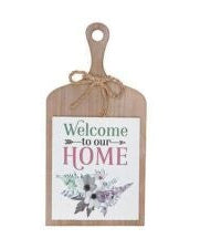 A wooden paddle sign with the text 'Welcome to our HOME' printed on it, featuring a floral design and a rope hanger.