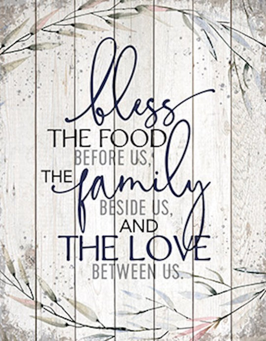 A plaque with a wooden background and the phrase 'bless the food before us, the family beside us, and the love between us' written in a cursive script.