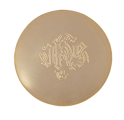 A gold-colored metal paten with the Christian symbol IHS engraved on its surface.