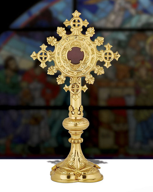 A brass reliquary with ornate designs, featuring a 3-inch opening at the top for displaying relics, placed against a blurred background with a religious painting.