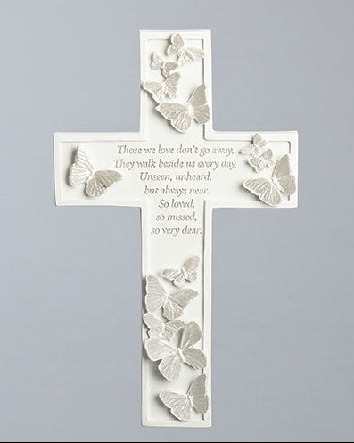 A white memorial wall cross with butterfly designs and an inscription that reads 'There we love don't go away, they walk beside us every day, unseen, unheard, but always near, so loved, so missed, so very dear.'.