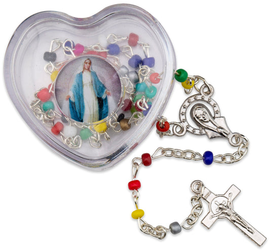 A multi-colored metal rosary with silver tone metal accents, displayed in a clear plastic heart-shaped box with a picture of Our Lady of Grace on top. The rosary beads are visible outside the box, attached to a cross.
