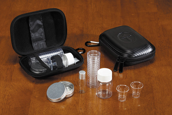 A portable communion set displayed with a zippered vinyl case, plastic cups, an aluminum box, glass oil vial, and plastic bottle, all laid out on a wooden surface.