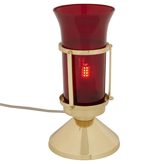 A sanctuary lamp with a high polished brass base and a ruby glass globe, pluged into a white cord.