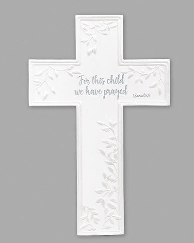A white wall-mounted cross with text from 1 John 4:10, 'For this child we have prayed'.