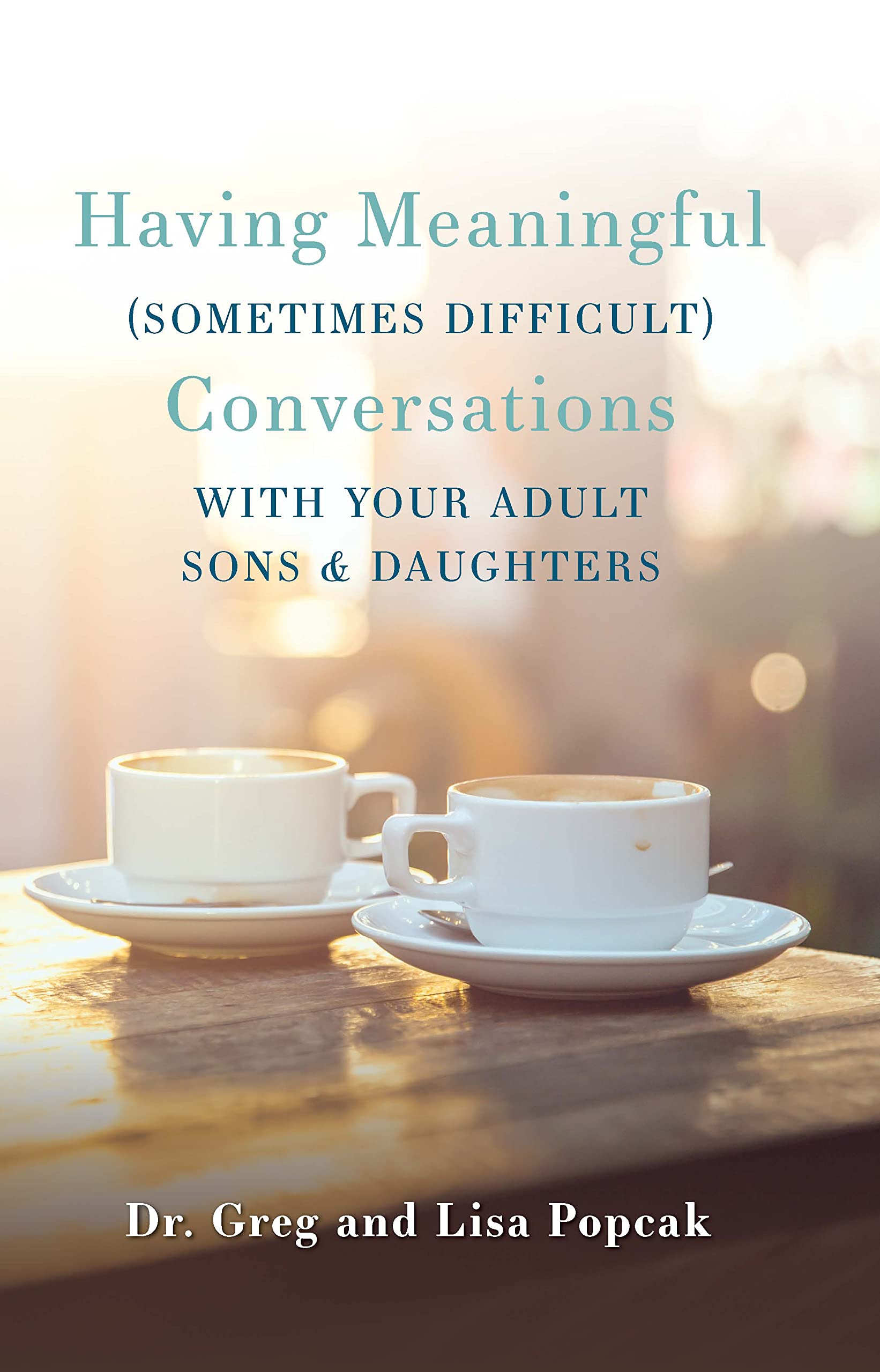 Two white coffee cups on saucers, with a book titled 'Having Meaningful (sometimes difficult) Conversations with Your Adult Sons & Daughters' by Dr. Greg & Lisa Popcak placed above them.