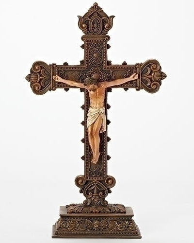 A tabletop crucifix made of resin, featuring intricate carvings and a figure of a person crucified on a cross with a decorative backdrop.