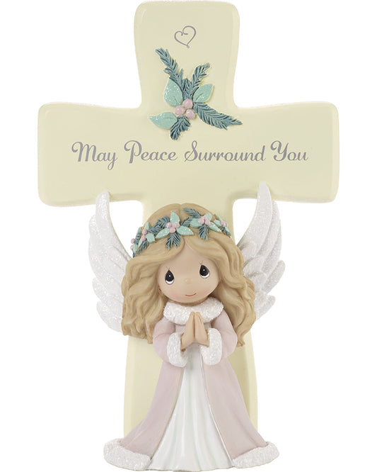 A beige resin cross with a white background, featuring a peaceful angel figure in the center, with green and pink details on the angel's dress, and the text 'MAY PEACE SURROUND YOU' on the cross.