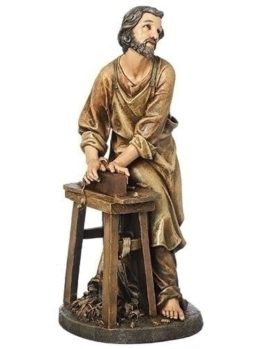 A statue of St. Joseph the Worker depicted as a carpenter, sitting at a workbench with tools, primarily in brown tones.
